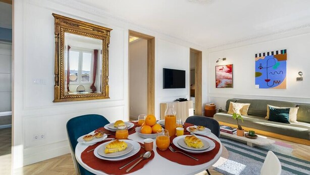 A dining area with a table set for breakfast, a large mirror, and a sofa in the background. - Historic Centre Modern Masterpiece w/ River Views (Lisboa)