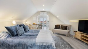 Ett rymligt sovrum på vinden med en stor säng, en soffa, en tv och en matplats.