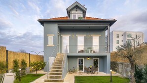 Uma casa de dois andares com varanda, escadaria e um espaço de pátio com móveis para área externa.