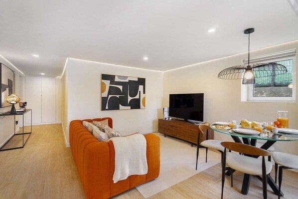 Una sala de estar moderna con un sofá, televisión, mesa de comedor y un cuadro en la pared.