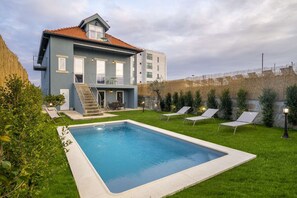 A modern two-story house with a swimming pool, a balcony, and a well-maintained garden.