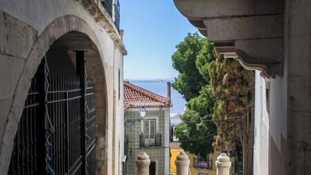 A narrow street with stone buildings, a metal gate, and a tree. - Central Alfama Hideaway perfect to explore Lisbon (Lisboa)