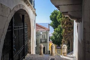 Une rue étroite bordée d’immeubles en pierre, avec une grille en métal et un arbre.