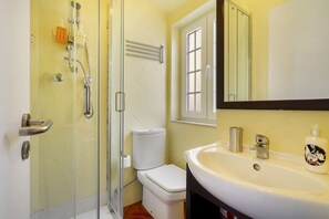 A bathroom with a glass-enclosed shower, a toilet, a sink with a mirror, and a window. - Central Alfama Hideaway perfect to explore Lisbon (Lisboa)