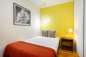 A bedroom with a bed, a bedside table with a lamp, a framed artwork on the wall, and a yellow accent wall. - Central Alfama Hideaway perfect to explore Lisbon (Lisboa)