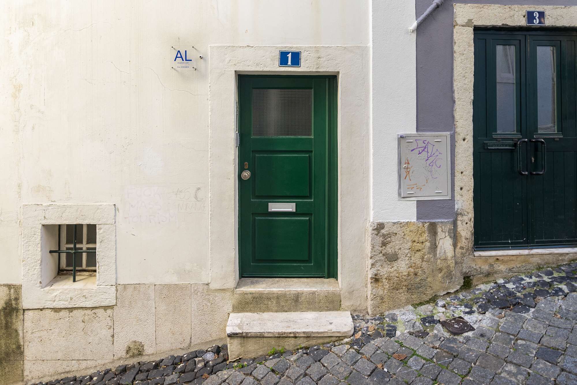 Ein Gebäude mit einer grünen Tür, die mit der Nummer 1 gekennzeichnet ist, einem kleinen Fenster mit einem Metallgitter und einem steinernen Tritt, der zur Tür führt.