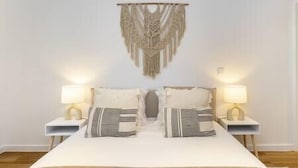 A bedroom with a bed, two bedside tables with lamps, and a macrame wall hanging.
