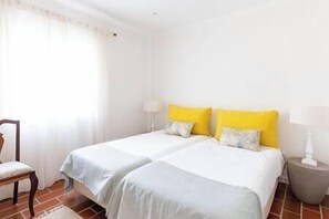 Una habitación con dos camas, una silla y una mesita de noche con lámpara.