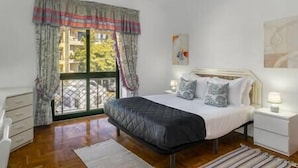 A bedroom with a bed, bedside tables, a window with curtains, and a painting on the wall.