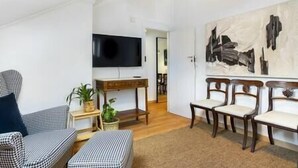 Uma sala de estar com televisão de tela plana, um quadro e uma área de jantar com cadeiras e mesa.