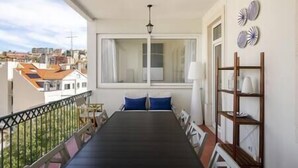 Un balcón con una mesa y sillas, vistas a edificios y una estantería con platos.