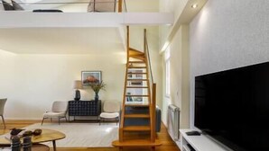 Una sala de estar moderna con una escalera espiral de madera, un televisor de pantalla plana y una zona de estar con una mesa de centro.