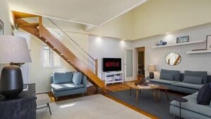 Un amplio espacio de estar con una escalera, un televisor de pantalla plana y dos sofás.