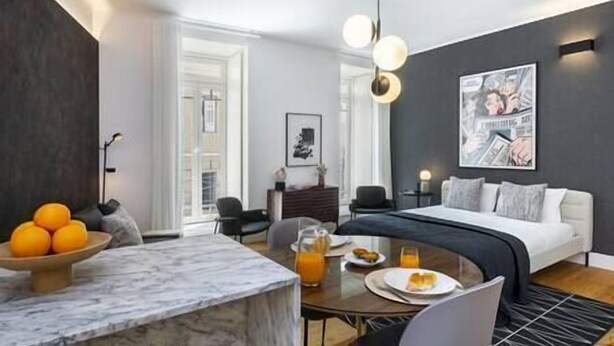 Ein modernes Hotelzimmer mit einem Bett, einem Esstisch mit Früchten, einem Couchtisch und einem großen Fenster.