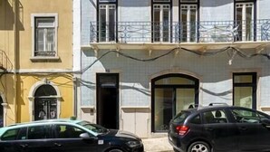 Ein Gebäude mit Balkon, einer Tür und zwei parkenden Autos.