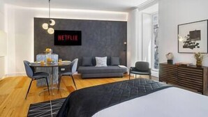 Ein modernes Hotelzimmer mit einem Bett, einer Couch, einem Schreibtisch mit Stuhl, einem an der Wand montierten Fernseher und einem großen Fenster.