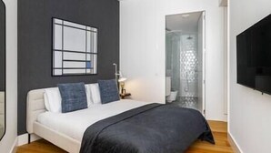 Ein modernes Schlafzimmer mit Bett, einem an der Wand befestigten Fernseher und einer Duschkabine.