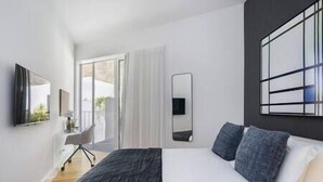 Ein modernes Schlafzimmer mit einem großen Bett, einem Schreibtisch und einem Stuhl. Eine Schiebetür führt zu einem Balkon.