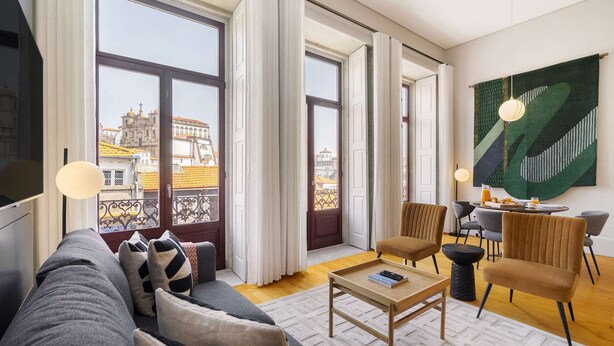 En moderne stue med sofa, stole, et sofabord og et spiseområde med udsigt til historiske bygninger.