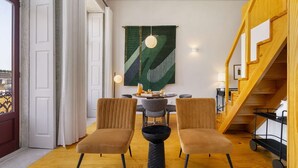 Et moderne spiseområde med et rundt bord, to stole og et stort abstrakt billede på væggen.