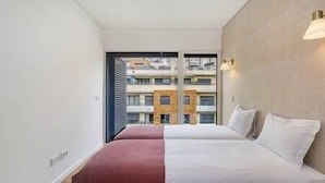 Habitación de hotel con dos camas, vista a un edificio con balcones y una lámpara en la pared.