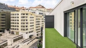 Un edificio moderno con terraza en azotea plana y un pequeño césped.