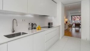 Una cocina moderna con armarios blancos, un lavamanos de acero inoxidable y una cafetera.