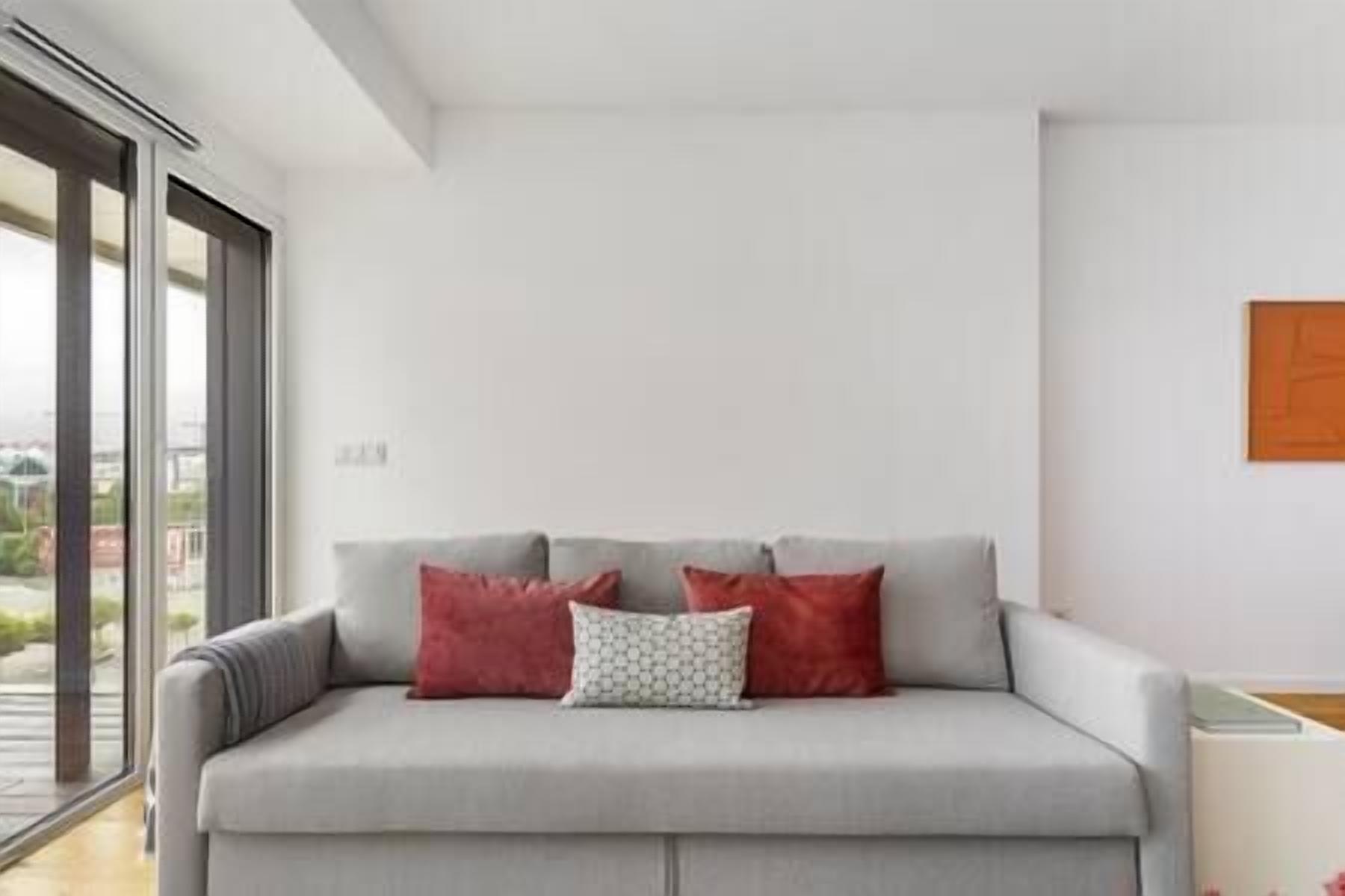 A modern living room with a grey sofa, two red cushions, and a patterned pillow.