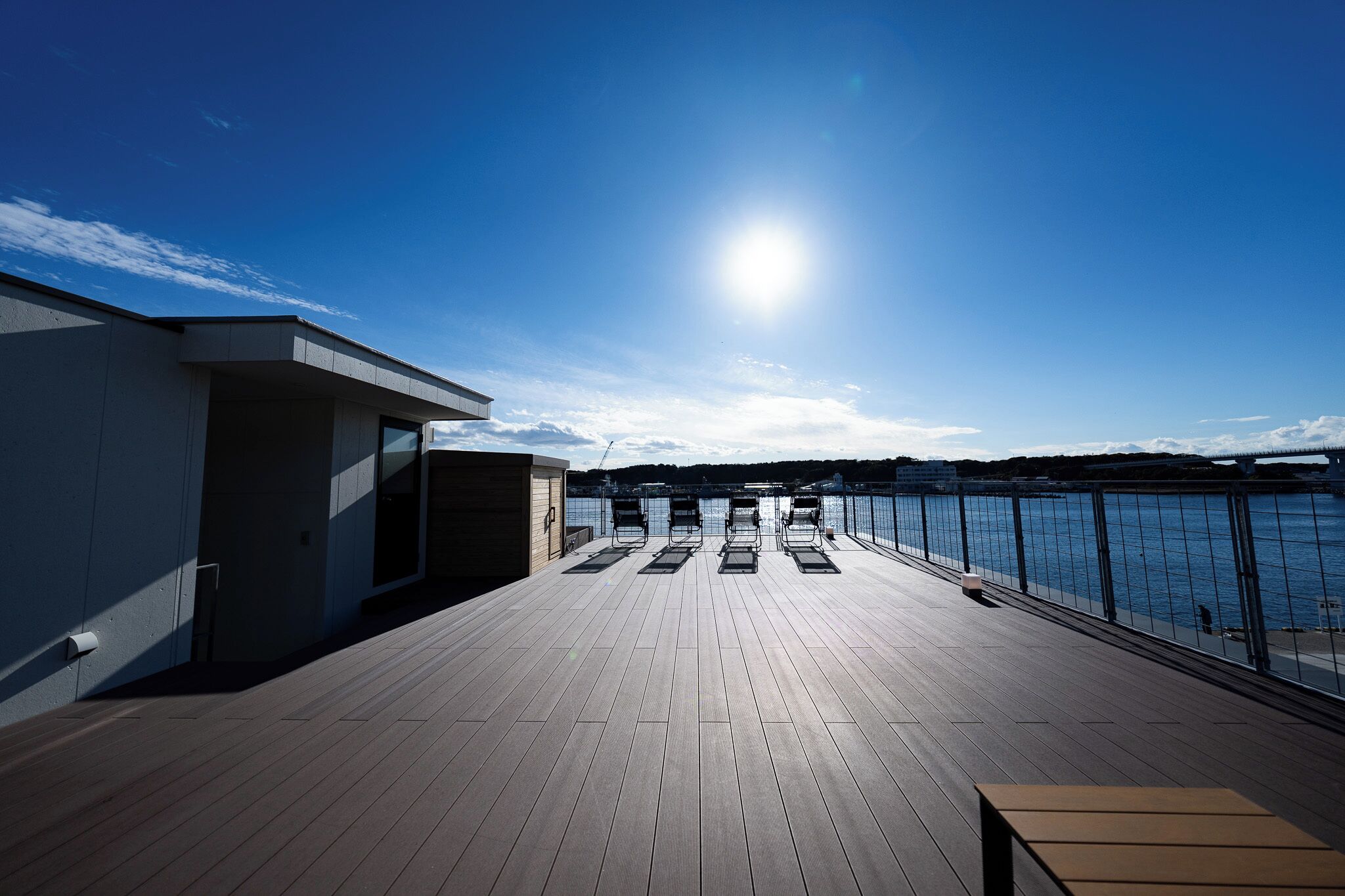 A wooden deck with a view of the water and a bridge in the distance.
