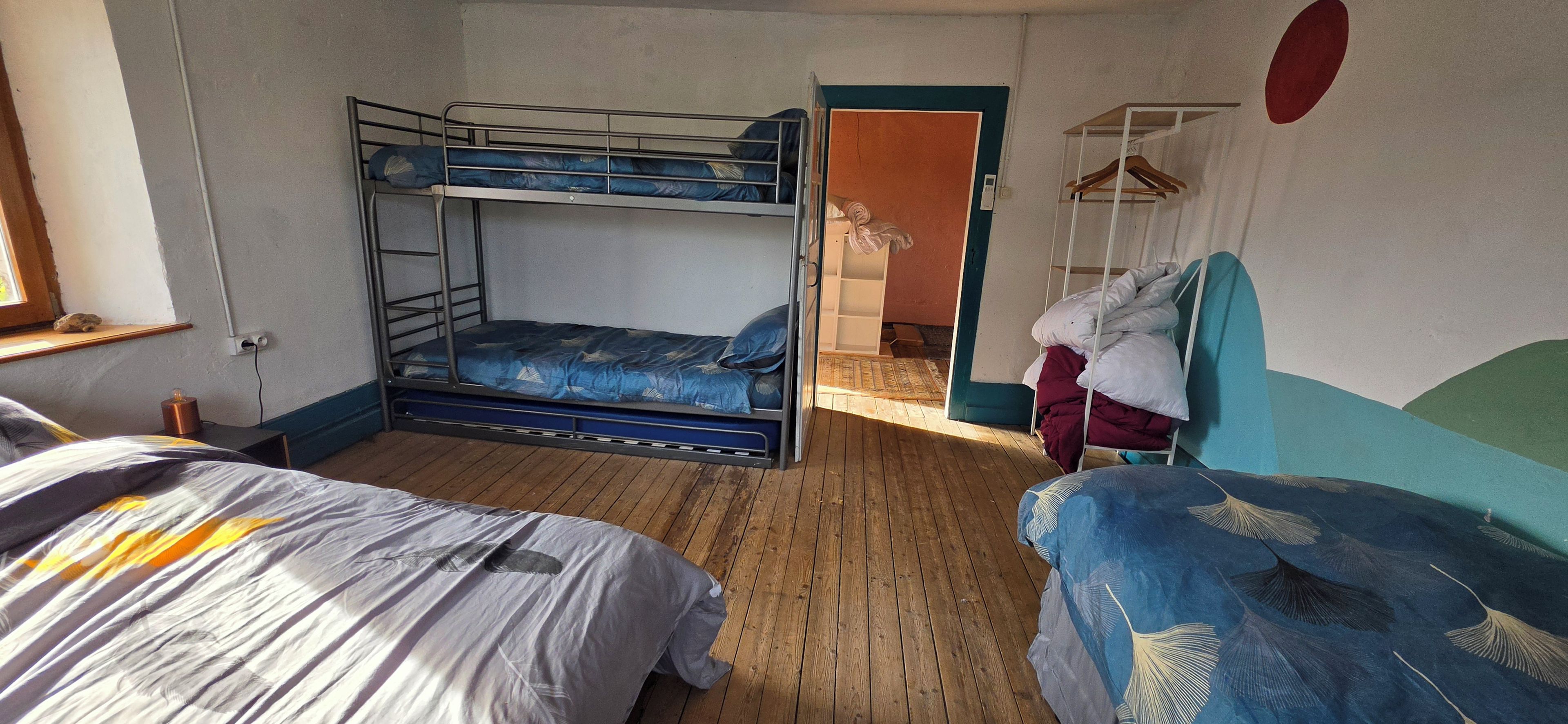 Et sovesalsværelse med køjesenge, trægulv og et garderobeskab med plads til ophængning.