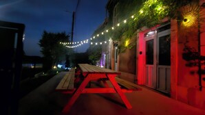 A nighttime outdoor setting with string lights, a wooden bench, and a building with a door.