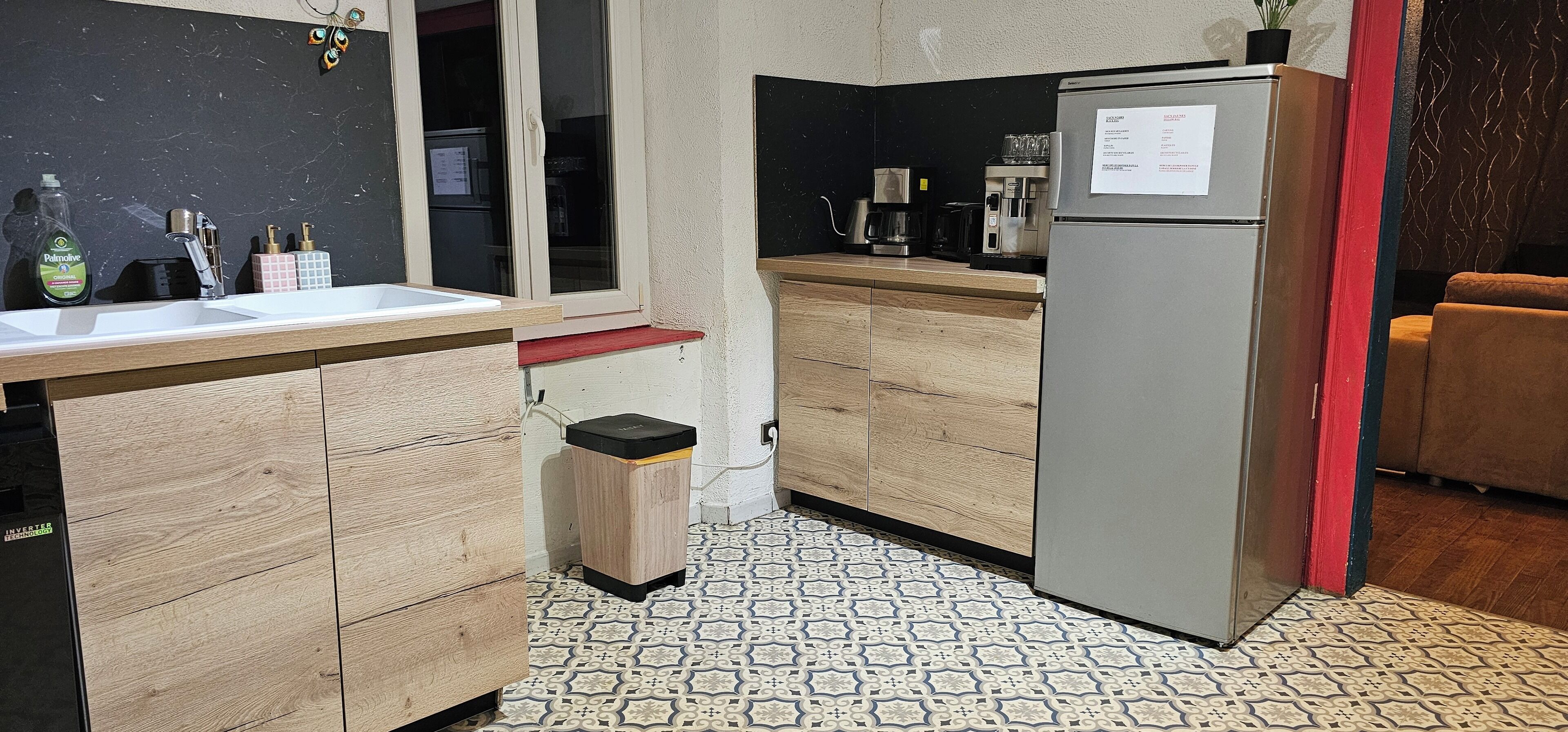 A compact kitchen with a refrigerator, coffee maker, and a small trash bin.