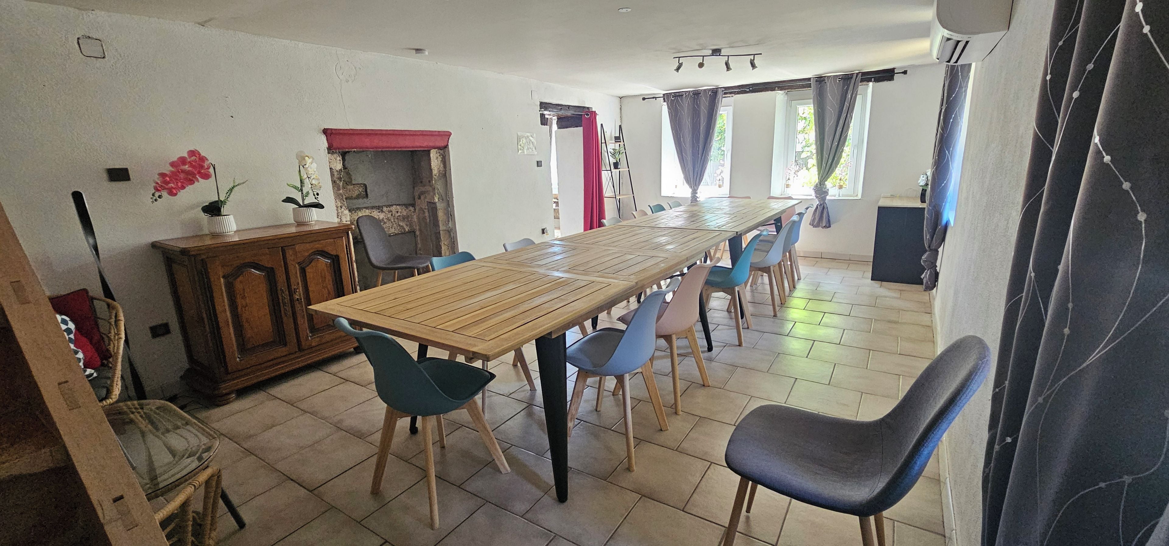A dining area with a long wooden table, blue chairs, a cabinet, and a fireplace.