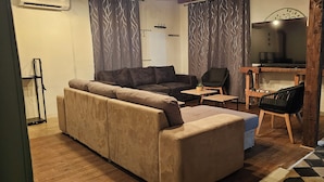 A living room with a beige sofa, a black chair, a small table, and a TV.