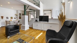 Amplia sala de estar con techo alto, una escalera, un comedor y un televisor sobre un mueble blanco.