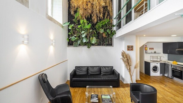 Una sala de estar moderna con un sofá de cuero negro, una mesa de centro transparente y un ventanal con vistas al cielo.