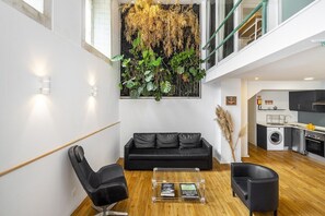 Un salon moderne avec un canapé en cuir noir, une table basse en verre et une grande fenêtre donnant sur le ciel.