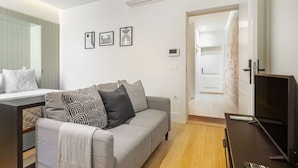 Una sala de estar moderna con un sofá gris, cojines estampados, un televisor de pantalla plana y una pequeña mesa.