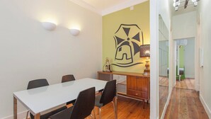 Een eetgedeelte met een witte tafel, vier stoelen, een houten kast en een muur met een geometrisch patroon.