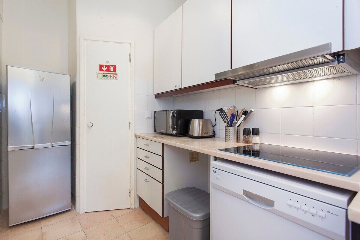 A compact kitchen with a stainless steel refrigerator, a microwave, a coffee maker, and a dishwasher.