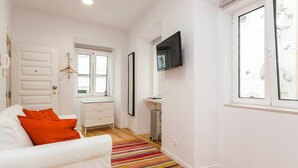 A modern, well-lit room with a white sofa, a colorful striped rug, a desk with a computer, and a mounted TV. - Hidden Gem I in Alfama perfect to explore Lisbon (Lisboa)