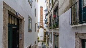 Un estrecho callejón flanqueado por edificios, un camino adoquinado y una chimenea alta a lo lejos.