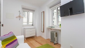 Un dormitorio moderno y bien iluminado con un aparador blanco, un espejo grande, un radiador y un televisor montado en la pared.