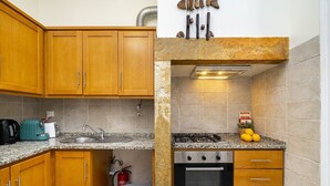 Una cocina compacta con armarios de madera, encimera de granito, cocina a gas y horno de acero inoxidable.