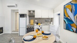 Una cocina moderna con armarios blancos, microondas, estufa y fregadero. Hay una mesa de comedor con platos y vasos, y un cuadro en la pared.
