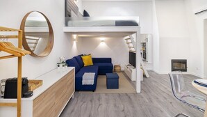 Un espacio habitable moderno y compacto con una cama individual superpuesta, un sofá, una mesa de centro y un televisor.