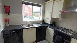 Cocina compacta con lavadora, lavavajillas, estufa y ventana con vistas al exterior.