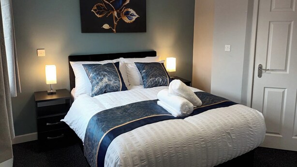 Habitación de hotel con una cama, dos mesitas de noche, una obra de arte en la pared y una puerta.