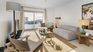 Ett modernt hotellrum med en soffa, en fåtölj och ett litet soffbord. Det finns ett stort fönster med utsikt över staden.