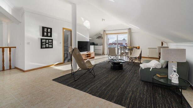 A spacious living area with a high ceiling, a large window, and a cozy seating arrangement.